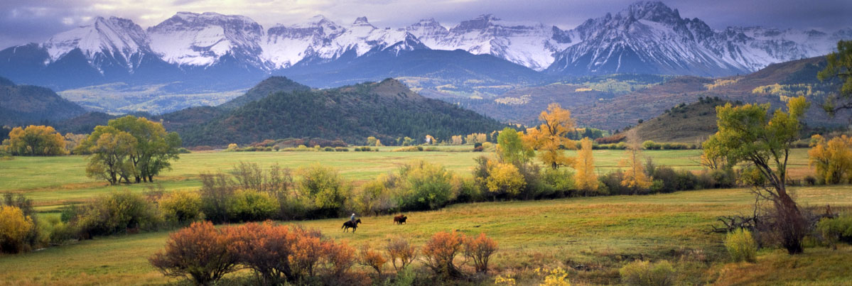 Two riders on horseback in front of beautiful, snowy mountains